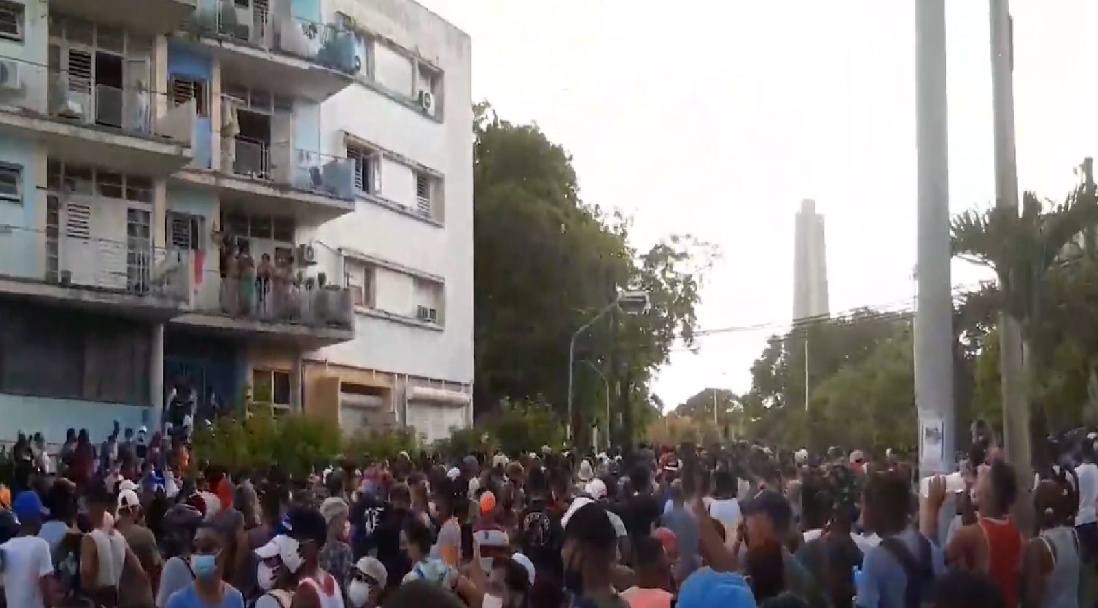 Una multitud llena una avenida de La Habana; al fondo, un monumento alto y vecinos asomados a los balcones.