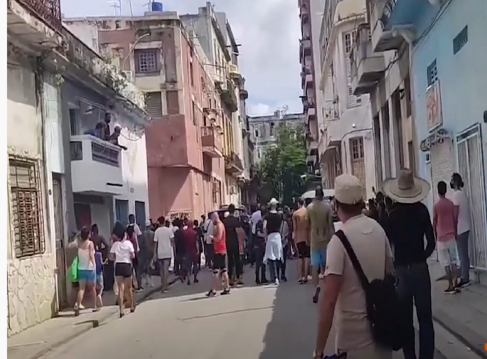 Decenas de personas caminan por una calle estrecha de La Habana entre edificios de varias plantas.