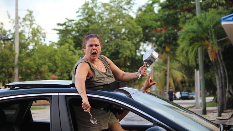 Una mujer asomada por la ventanilla de un coche en marcha golpea una cazuela con una cuchara.