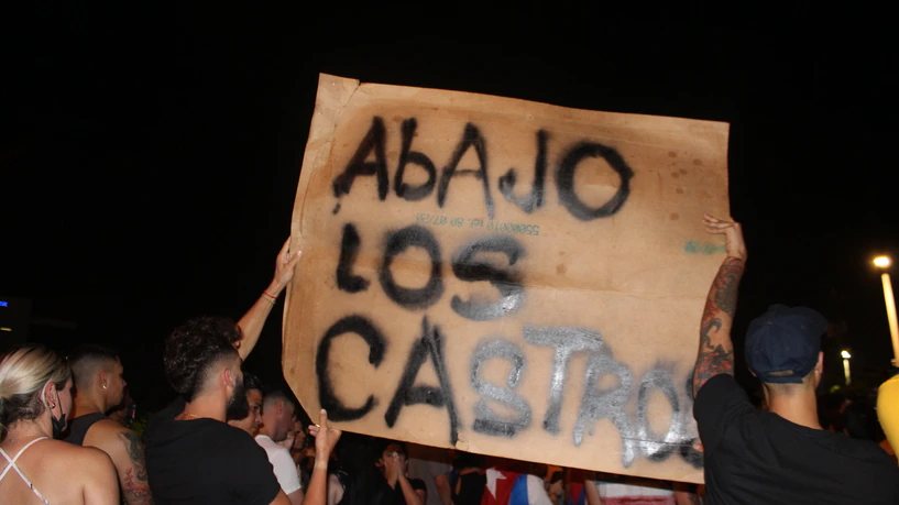 Varias personas sostienen en alto un cartón pintado con las palabras «Abajo los Castros», de noche.